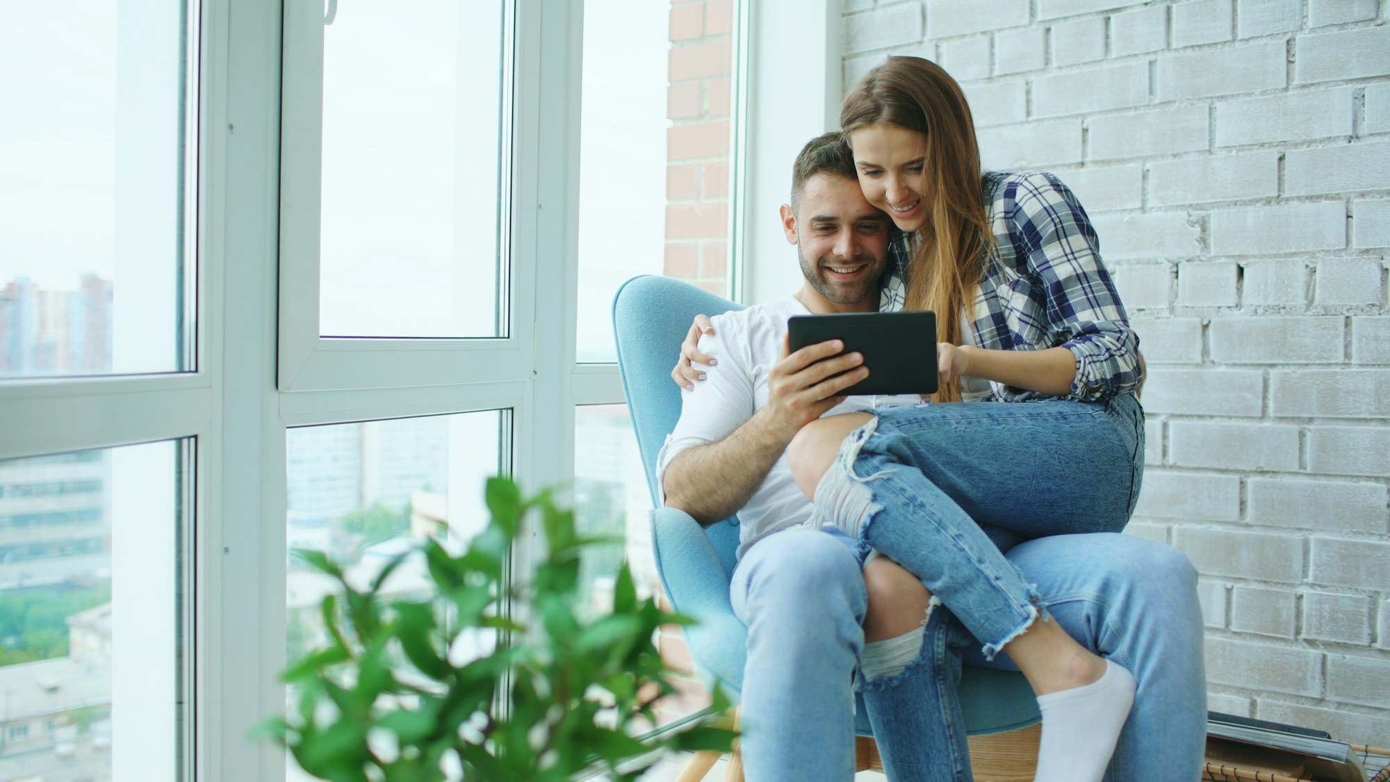 Couple sitting together by a bright window looking at a tablet