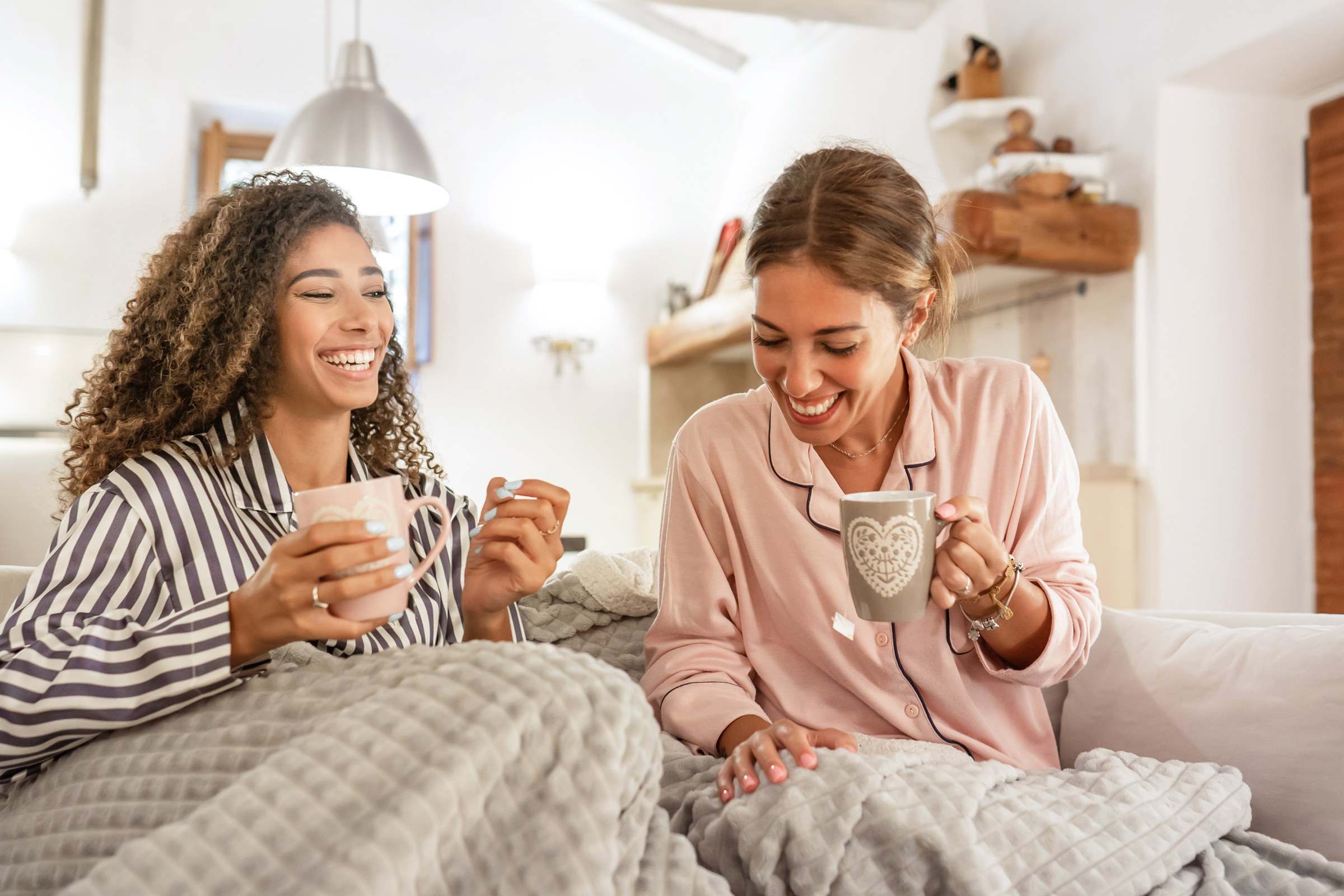 Two women laughing together over coffee on the sofa
