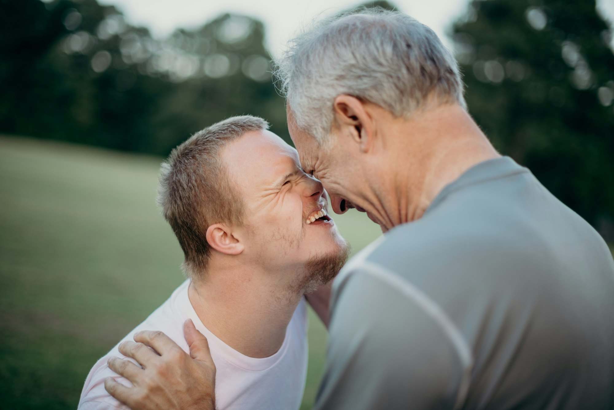 Father and his adult son with Down syndrome laughing forehead to forehead