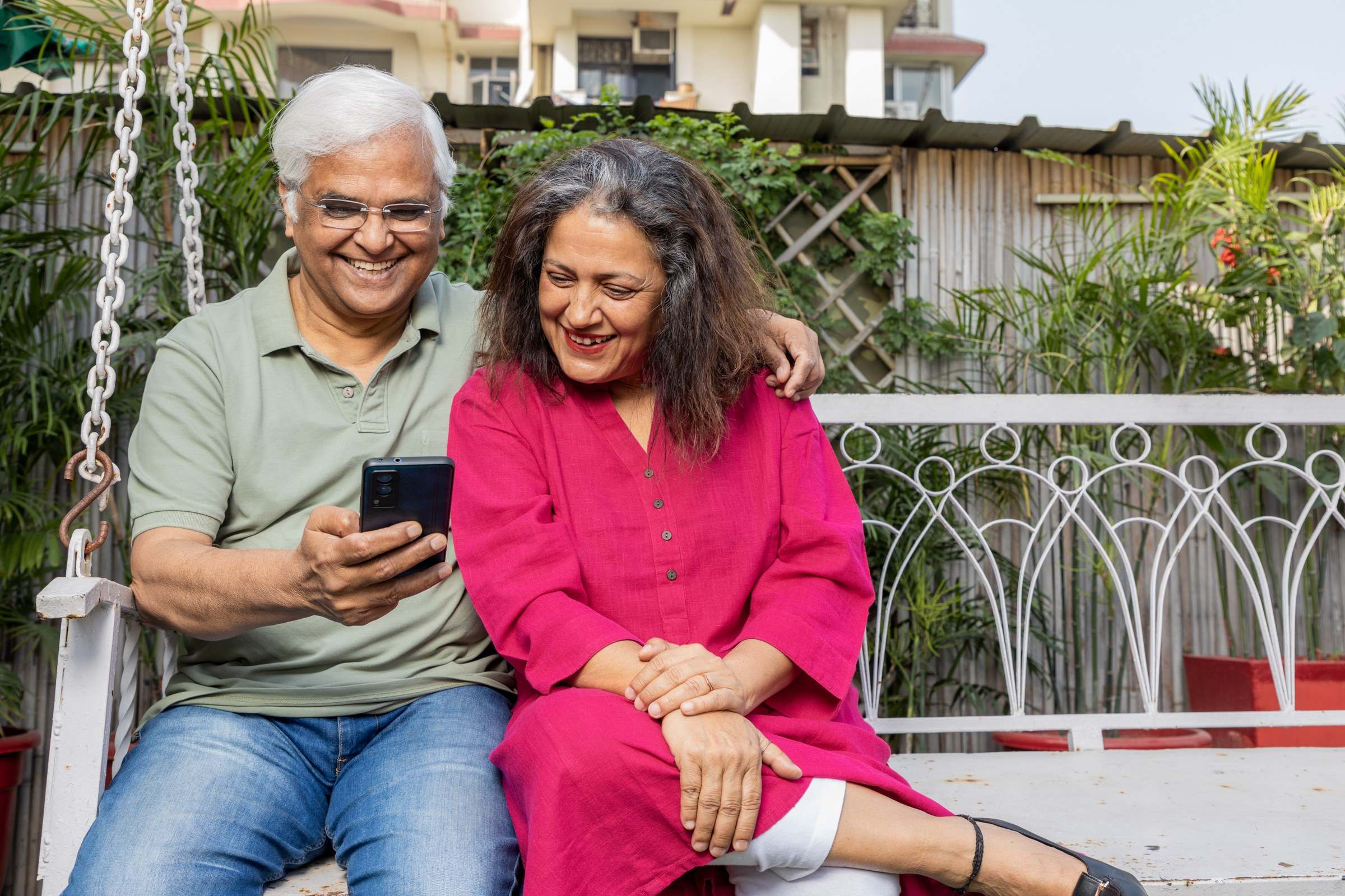 Older Indian couple smiling on a garden swing