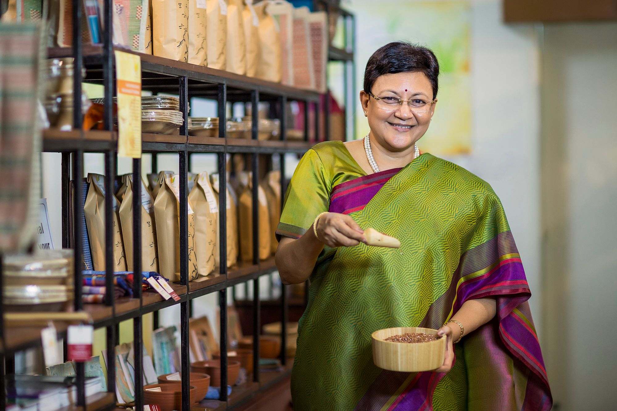 South Asian shop owner in a green silk sari smiling in her well-stocked store